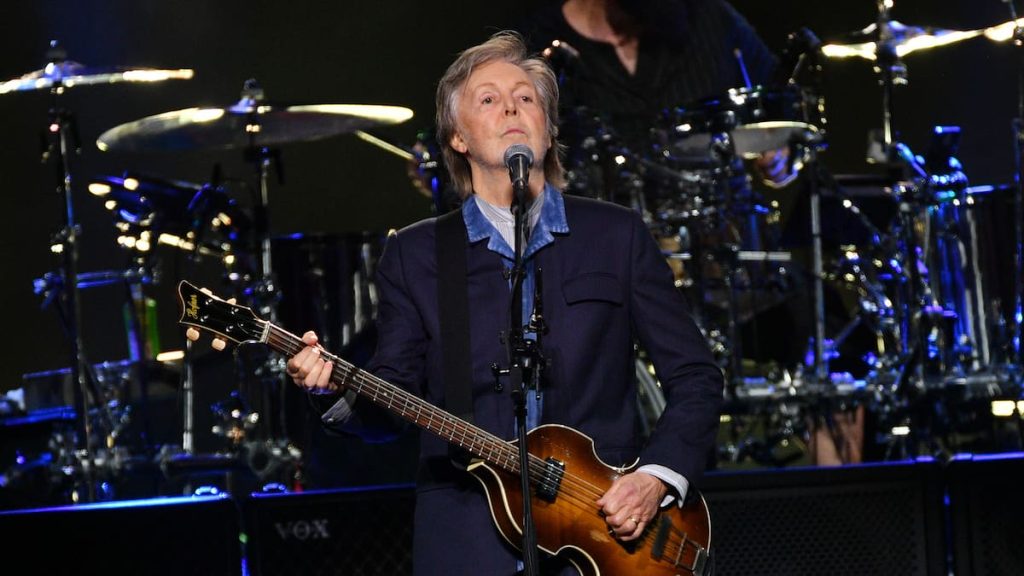 Paul McCartney sonriendo, con un micrófono, en una actuación en vivo.